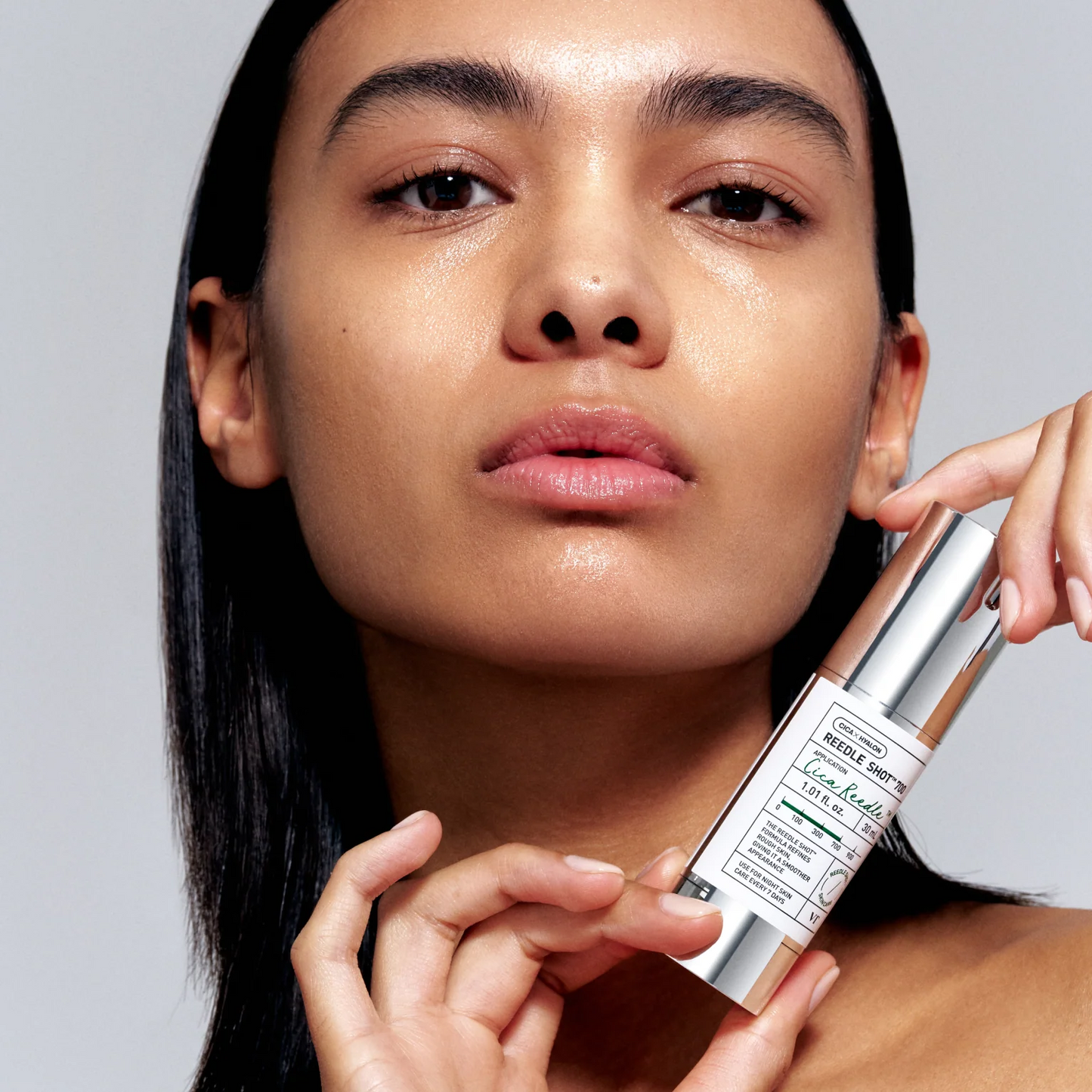 Woman holding a skincare product against a neutral background