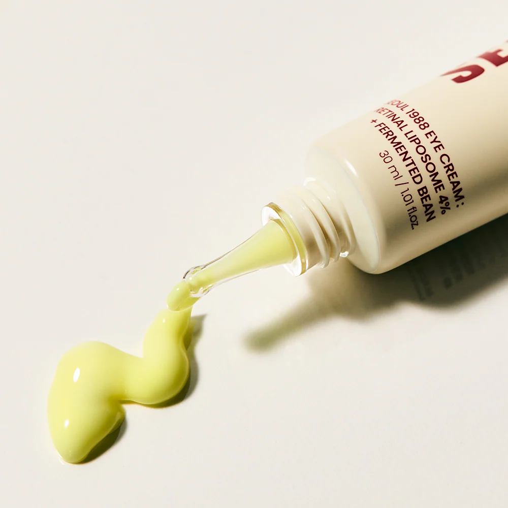 Eye cream bottle with green cream being squeezed out on a light background