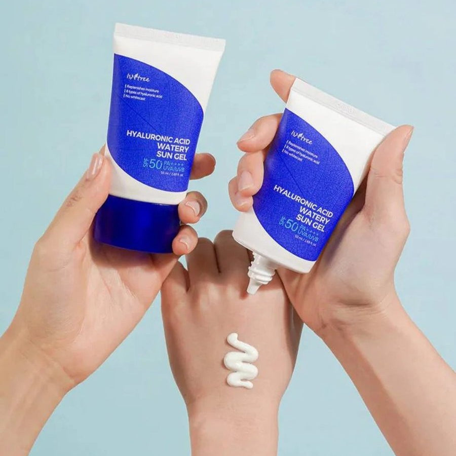 Two hands holding tubes of 'Hyaluronic Acid Water Gel' with a light blue background