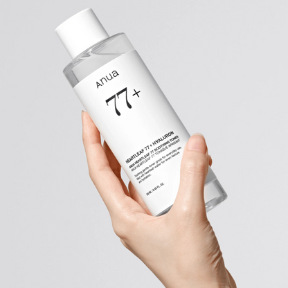 Hand holding a bottle of '77+' skincare product on a light gray background