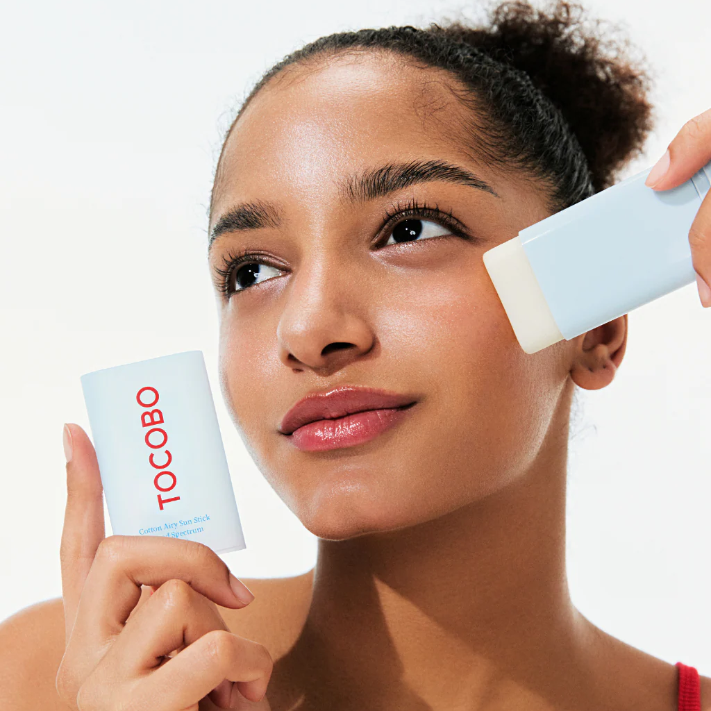 Woman applying sunscreen with a brush and Tocobo container on a white background